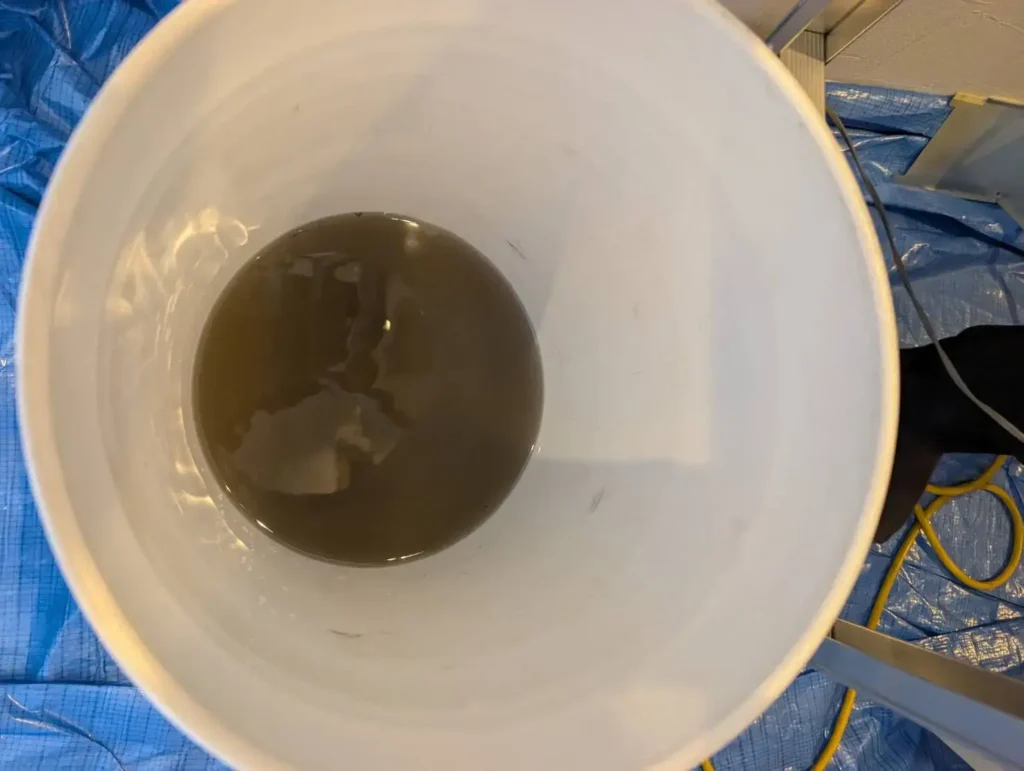 エアコンクリーニングで排出された汚れた洗浄水がバケツに溜まっている様子の写真。