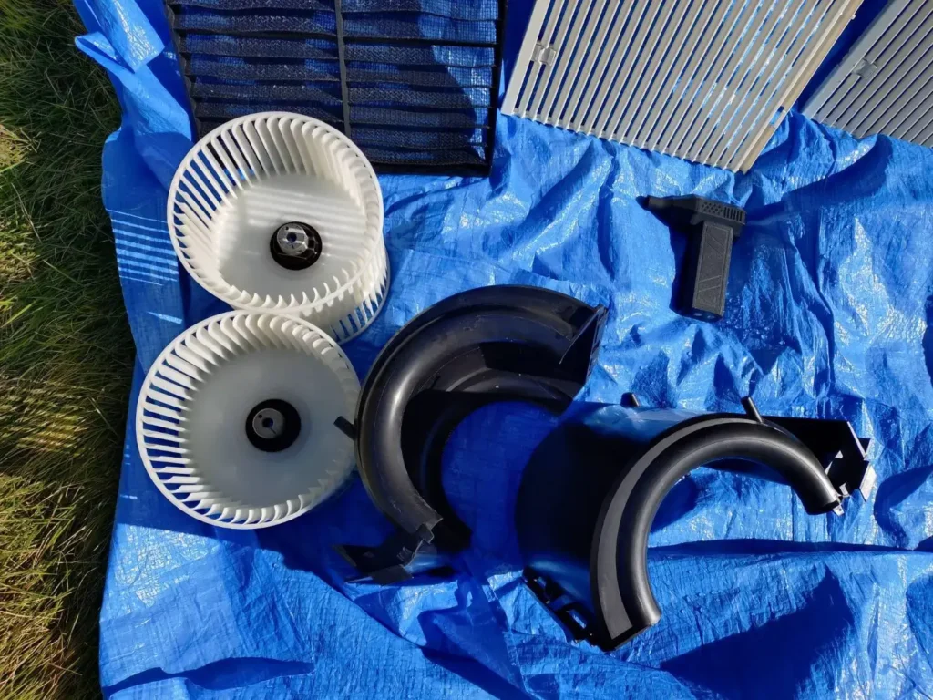 取り外した天井埋め込み型エアコンのファンやカバー、フィルターなどの部品をブルーシート上に並べた写真。