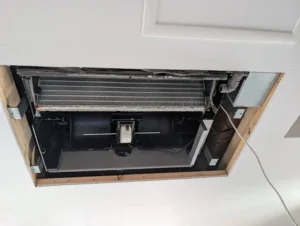 天井埋め込み型エアコンのパネルを外し、内部の熱交換器とファンが露出した状態。メンテナンスや清掃の作業前の様子を写した写真。