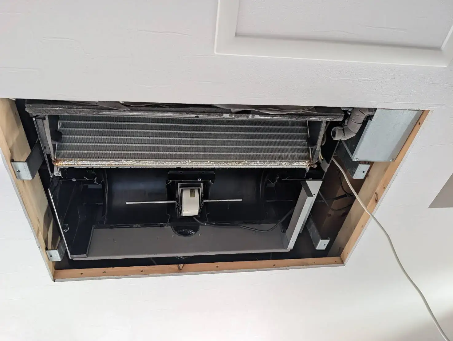 天井埋め込み型エアコンのパネルを外し、内部の熱交換器とファンが露出した状態。メンテナンスや清掃の作業前の様子を写した写真。