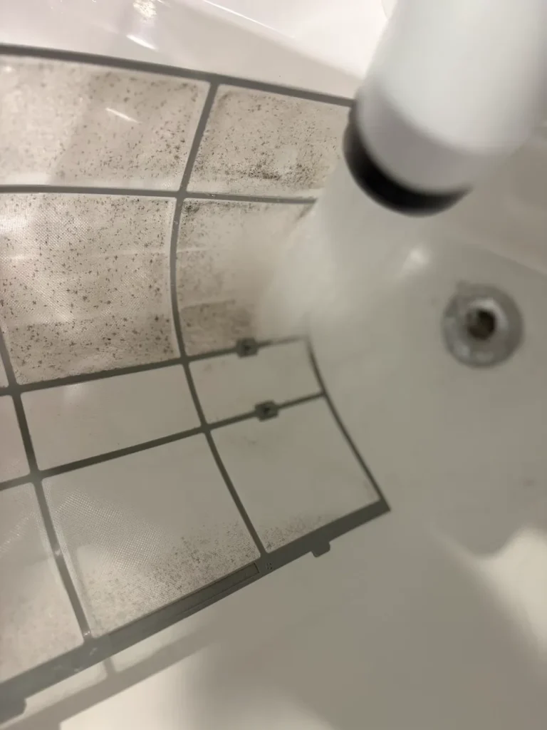 エアコンフィルターを水で洗ってホコリを落としている様子