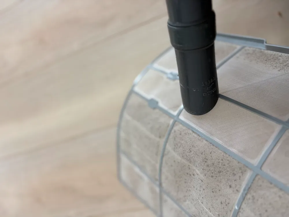 エアコンフィルターのホコリを掃除機で吸い取って掃除している様子